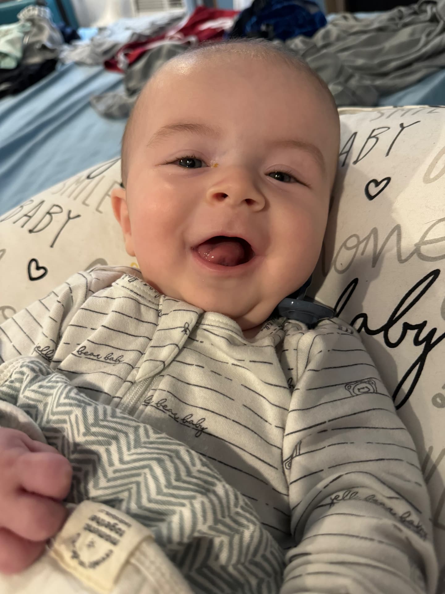 Baby Brayden laughing with his tongue out, wrapped in a striped sleeper