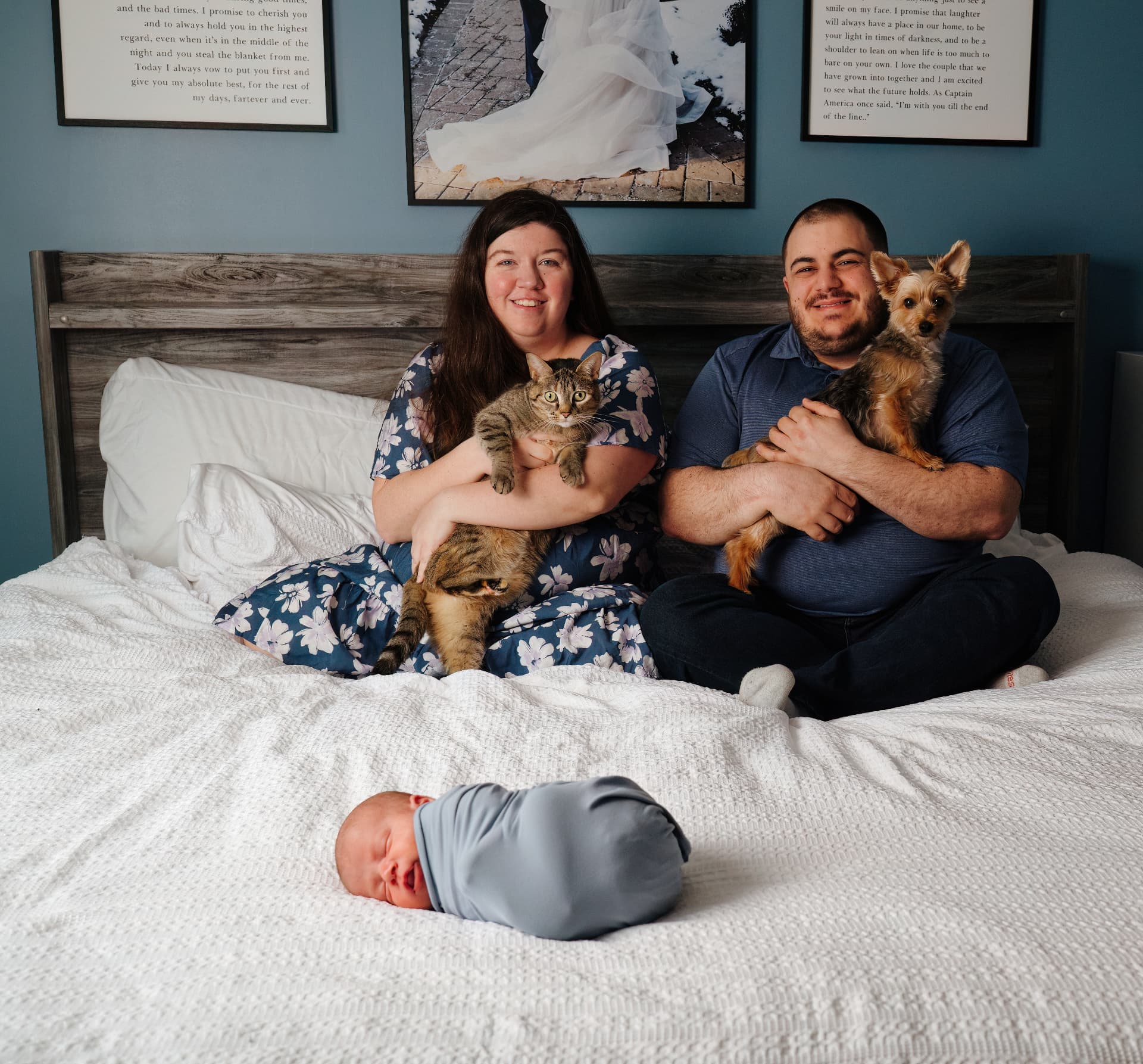 Amber and Giovanni Mio on a bed with their cat and dog and baby Brayden swaddled in front