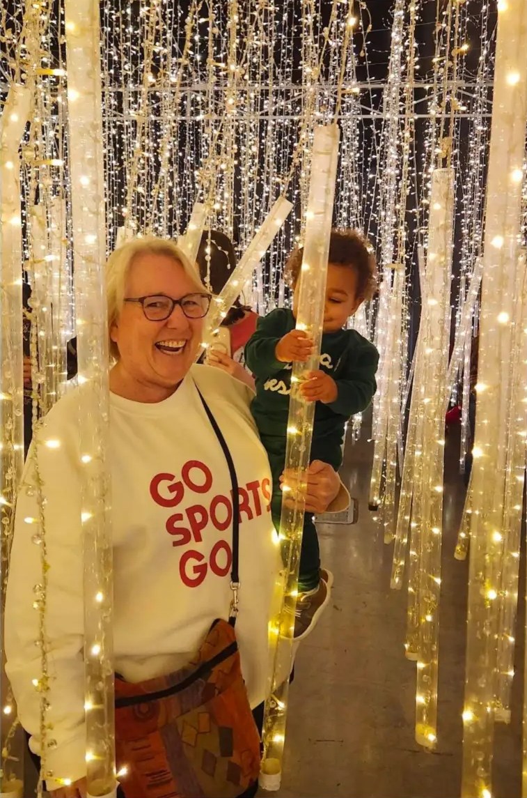 Susan Krolikowski laughing among twinkling light columns with a toddler