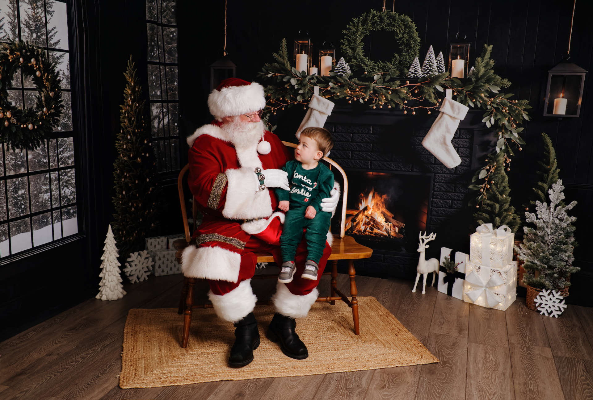Brayden in green velvet sitting on Santa's lap by a fireplace, looking up at him